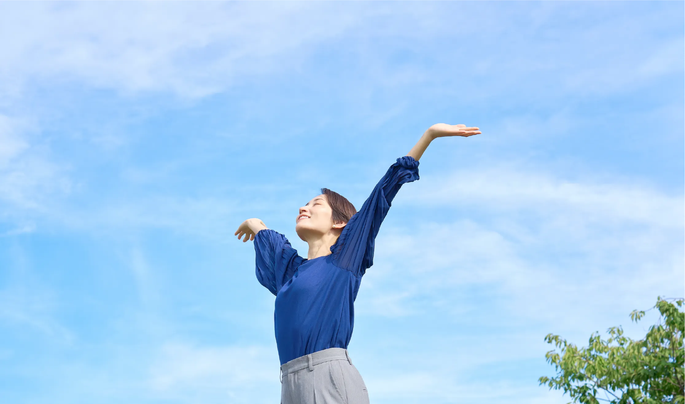 青空の下で両手を広げる女性